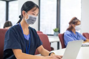 A nurse wearing a PPE mask reading her computer screen